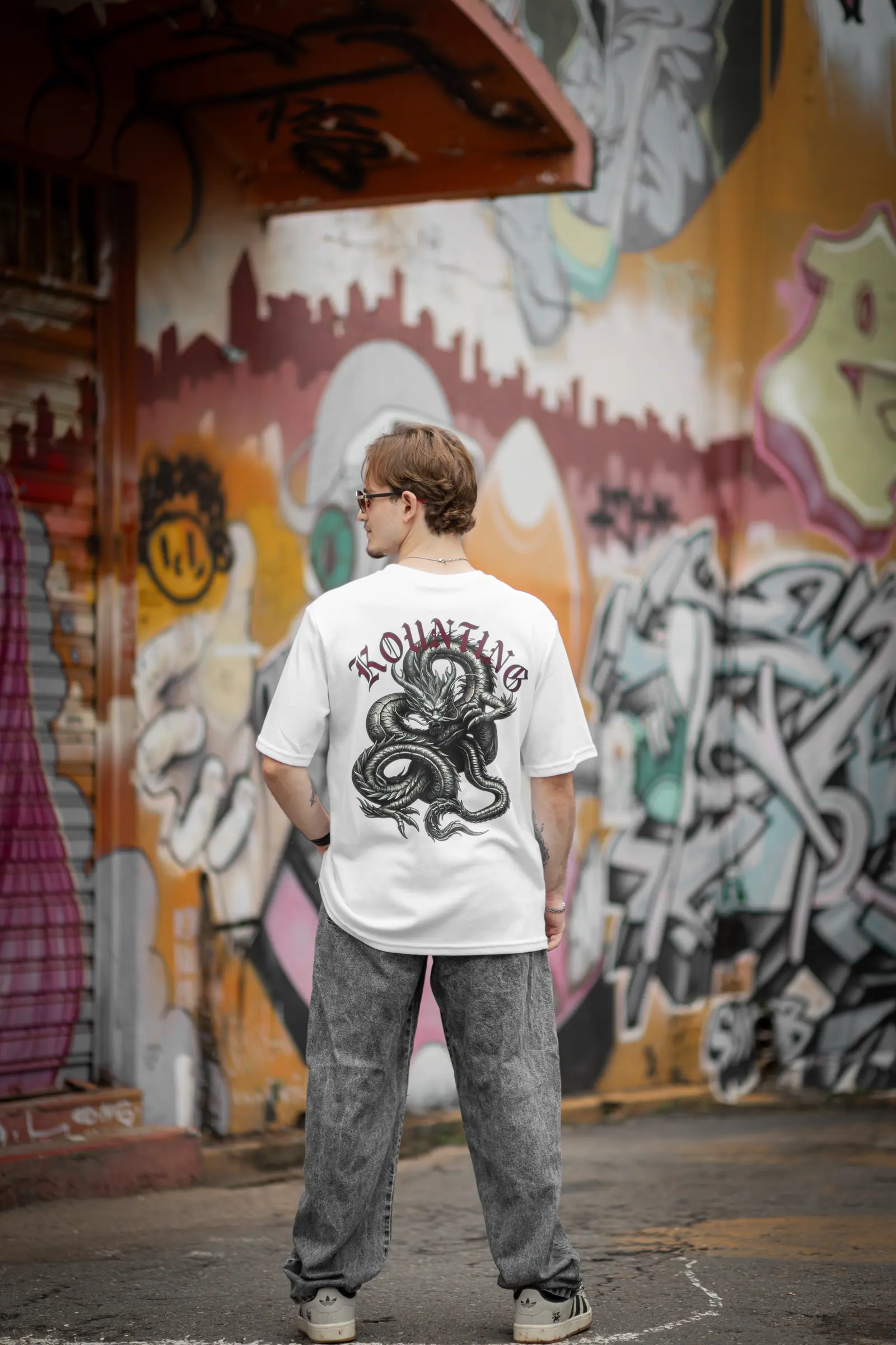 Costas da camiseta branca Premium Dragão em frente a muro de graffiti